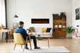 Amantii Symmetry Bespoke Extra Tall Electric Fireplace - installed on a white wall where a man reads in an armchair