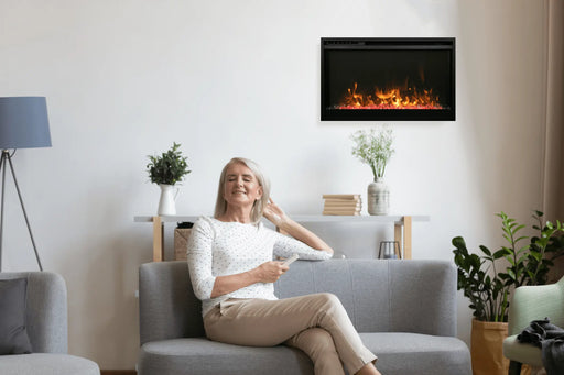 Amantii Traditional Xtra Slim Electric Fireplace - installed on a beige wall beside a woman on a sofa