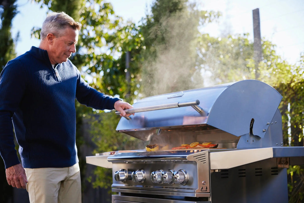Man lifting the hood of a Blaze LTE PRO 32" freestanding gas grill as smoke rises