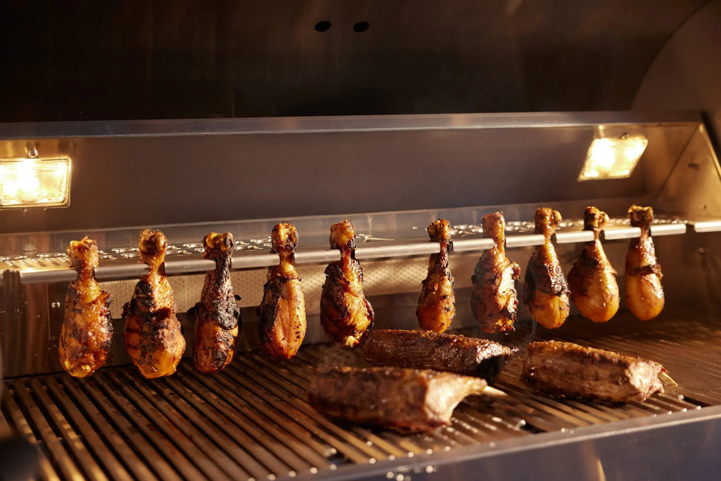 Chicken drumsticks hanging above the grates of a Blaze LTE PRO 40" gas grill with the interior lights on