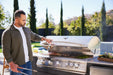 Man opening the hood of a Blaze LTE+ 40" gas grill built into an outdoor kitchen