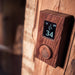 HUUM UKU wood sauna control mounted on a wood wall showing the temperature