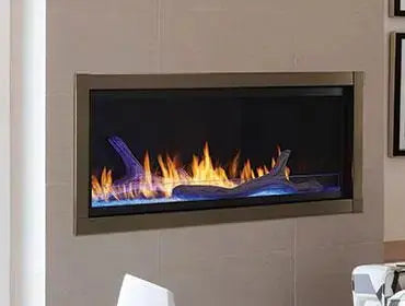 Monessen 72 in. Artisan vent free linear fireplace AVFL72 installed in a wall with a bronze-toned surround and blue-tinted flames