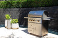 Wildfire Ranch Pro 36" gas grill in stainless steel with brushed bronze Designer Finish hardware on its cart on a patio against a dark wall, front view