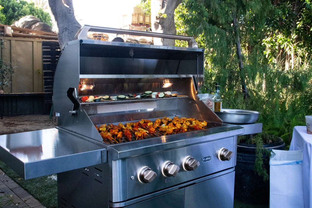Wildfire Ranch Pro 36" gas grill in stainless steel with brushed bronze Designer Finish hardware on its cart, hood open with food on the grates