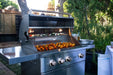 Wildfire Ranch Pro 36" gas grill in stainless steel with brushed bronze Designer Finish hardware on its cart, hood open with food on the grates