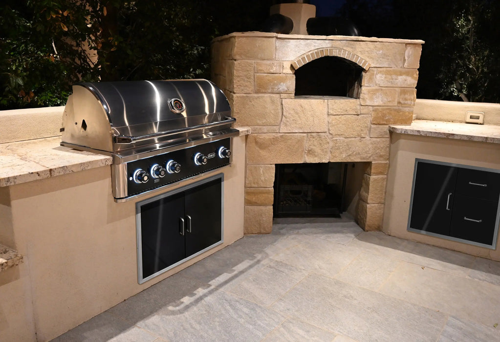 Wildfire Ranch Pro 42" gas grill in black stainless steel built into an island beside a pizza oven, at night