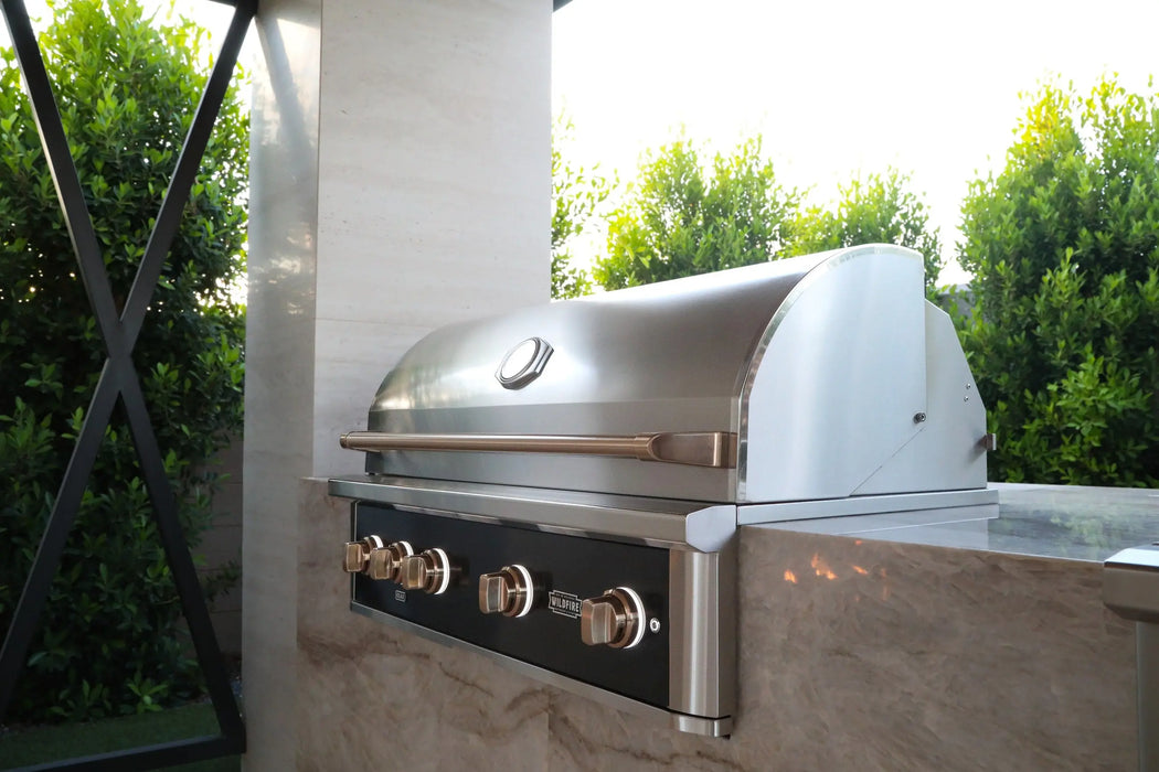 Wildfire Ranch Pro 42" gas grill in black stainless steel with brushed bronze Designer Finish hardware built into a stone island, hood closed