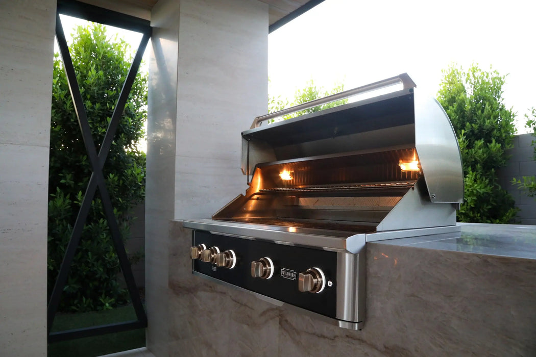 Wildfire Ranch Pro 42" gas grill in black stainless steel with brushed bronze Designer Finish hardware built into a stone island, hood open with the interior lights on