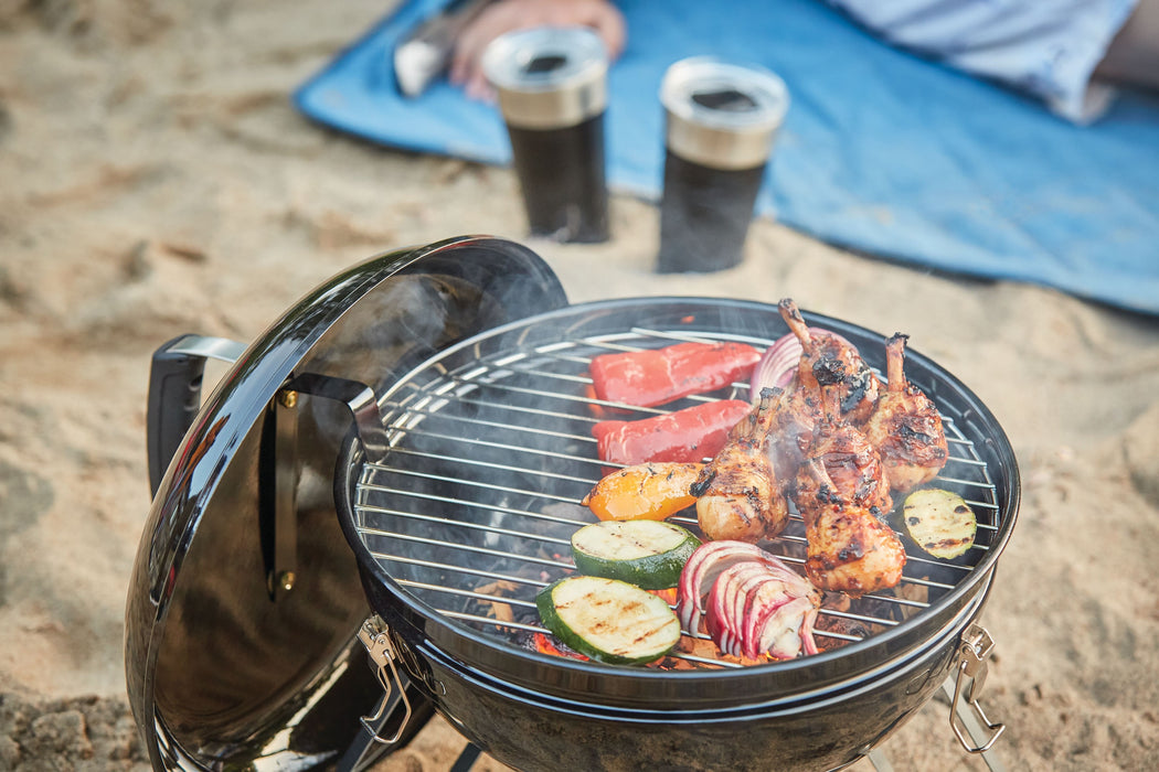 Napoleon 14" Portable Charcoal Kettle Grill - top view grilling meat and vegetables at a beach